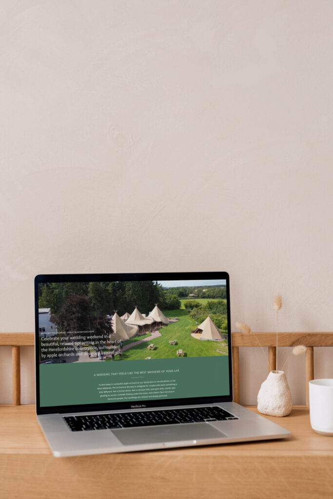 Laptop displaying The Orchard at Munsley wedding venue website, styled with off-white bud vases and dried flowers